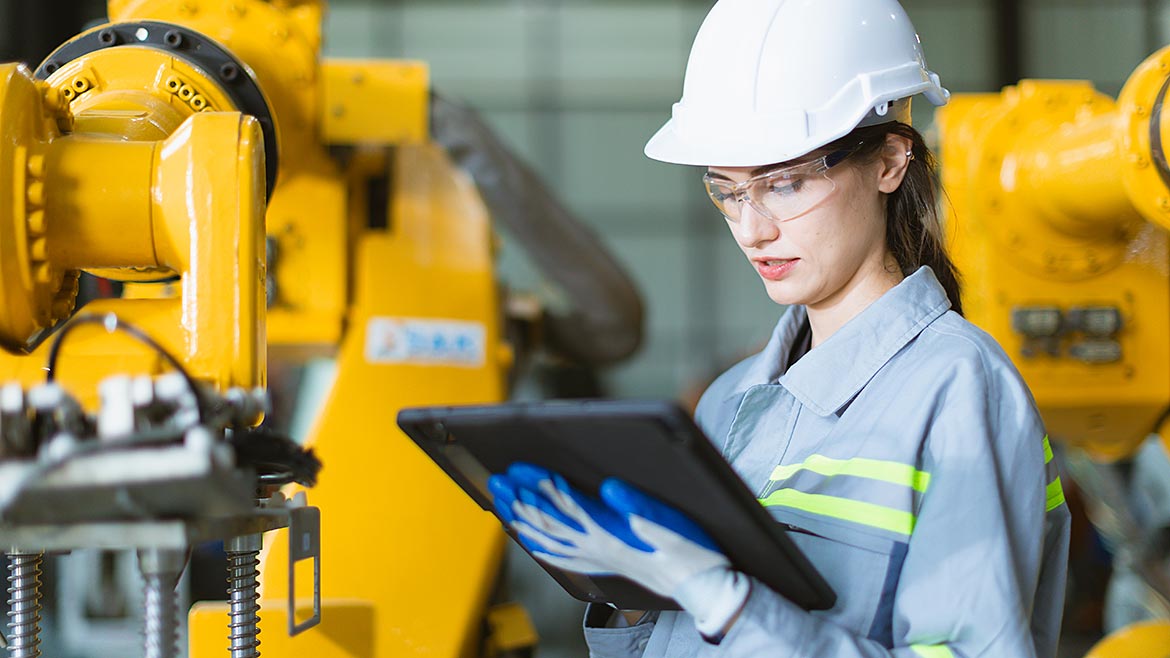 Female worker engineering staff work checking robot arm in assembly plant with tablet.